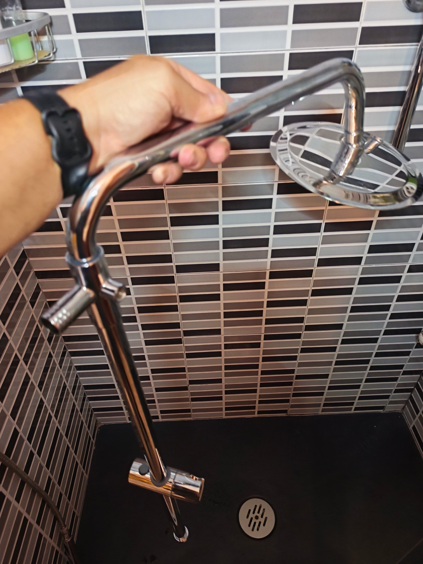 Barra de ducha cromada con rociador redondo en un baño de azulejo gris y negro