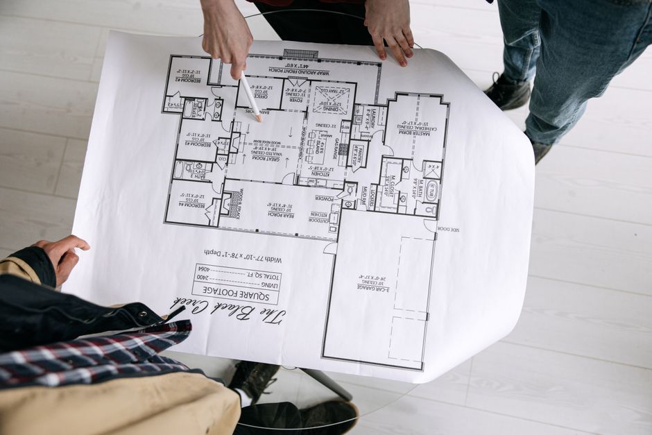 Planos de una obra sobre una mesa junto a un casco y un metro.