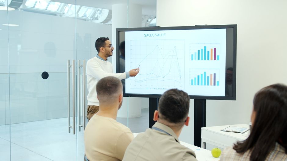 Un equipo comercial en una reunión mirando gráficos de resultados en una pantalla.